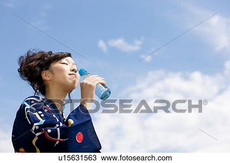 Stock Image - Young woman in Yukata drinking soda. Fotosearch