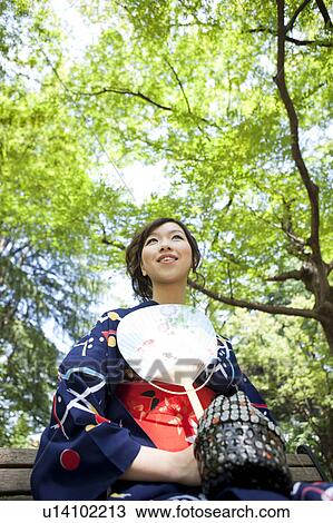 Stock Image - Young woman wearing Yukata sitting on bench. Fotosearch
