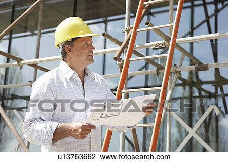 Stock Image - Architect Studying Plans Outside New Home. Fotosearch