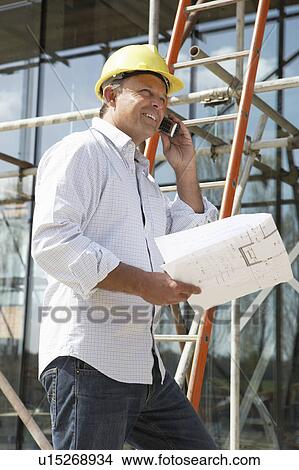 Picture - Architect With Plans Outside New Home Talking On Mobile Phone. Fotosearch
