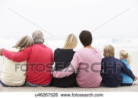 Stock Photograph - Back View Of Three Generation Family Sitting On Winter Beach Together. Fotosearch