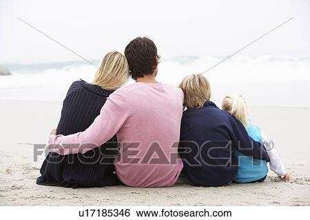 Stock Photograph - Back View Of Young Family Sitting On Winter Beach. Fotosearch