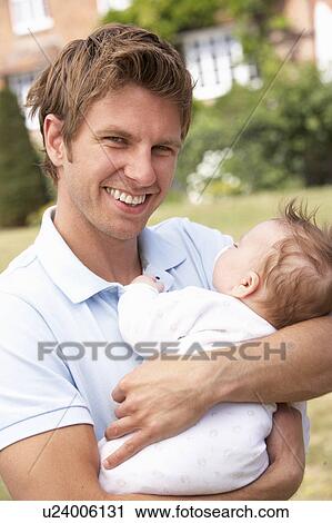 Stock Image - Close Up Of Father Cuddling Newborn Baby Boy Outdoors At Home. Fotosearch