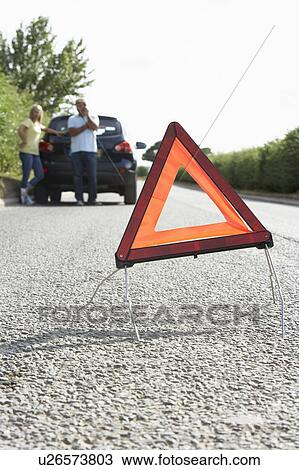 Stock Image - Couple Broken Down On Country Road With Hazard Warning Sign In Foreground. Fotosearch
