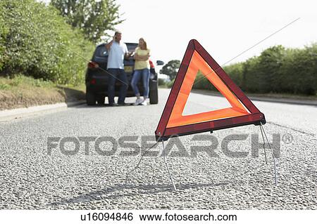 Stock Photograph - Couple Broken Down On Country Road With Hazard Warning Sign In Foreground. Fotosearch