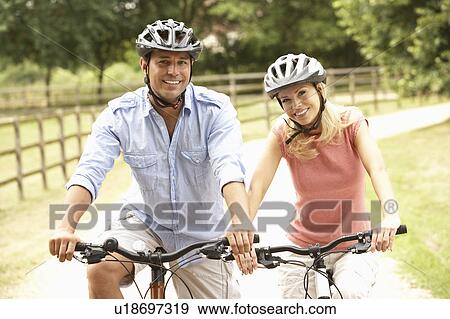 Couple Cycling In Countryside Wearing Safety Helmets View Large Photo Image Stock Photo - Couple Cycling In Countryside Wearing Safety Helmets. Fotosearch