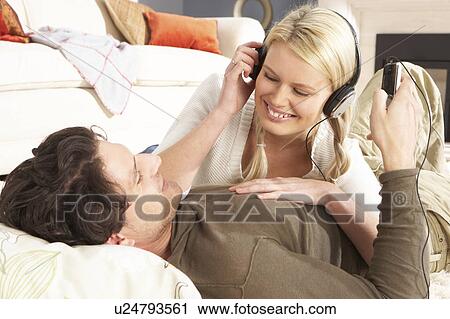 Stock Image - Couple Listening To MP3 Player On Headphones Relaxing Laying On Rug At Home . Fotosearch