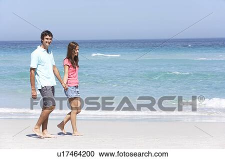 Stock Image - Couple On Holiday Walking Along Sandy Beach. Fotosearch