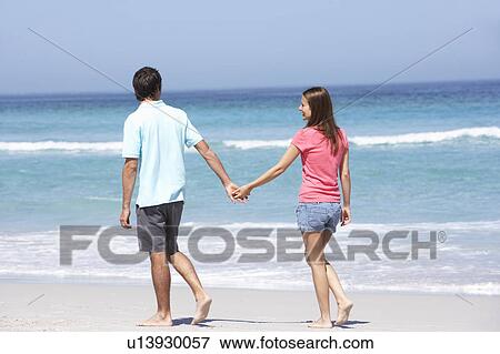 Stock Photo - Couple On Holiday Walking Along Sandy Beach. Fotosearch