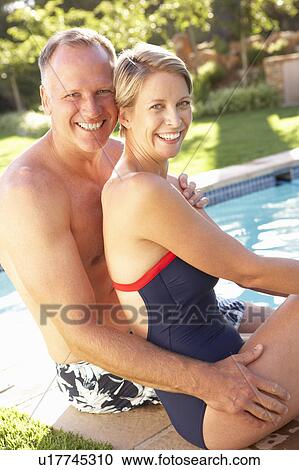 Stock Image - Couple Relaxing By Pool In Garden. Fotosearch