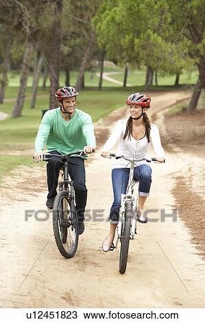 Couple riding bicycle in park View Large Photo Image Stock Image - Couple riding bicycle in park. Fotosearch