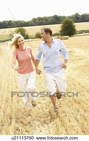 Stock Image - Couple Running Together Through Summer Harvested Field. Fotosearch