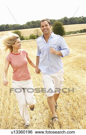Stock Photograph - Couple Running Together Through Summer Harvested Field. Fotosearch