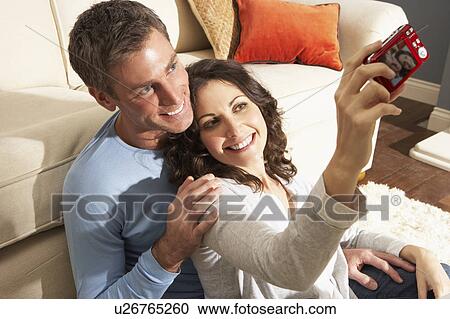 Stock Image - Couple Taking Photograph On Digital Camera At Home . Fotosearch