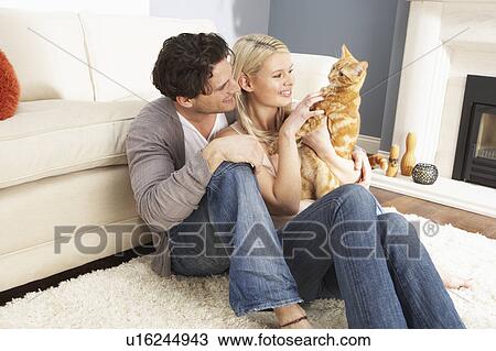 Stock Image - Couple Taking Playing With Pet Cat At Home . Fotosearch