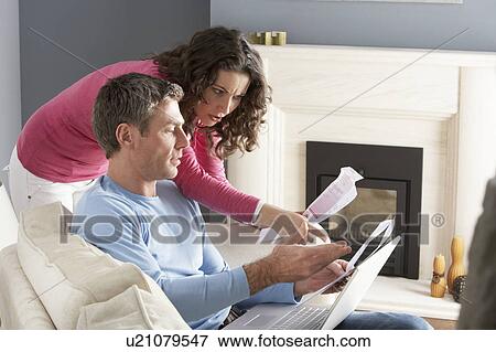 Stock Photo - Couple Using Laptop And Discussing Household Bills Sitting On Sofa At Home. Fotosearch