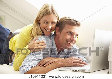 Couple Using Laptop Relaxing Sitting On Sofa At Home View Large Photo Image Stock Image - Couple Using Laptop Relaxing Sitting On Sofa At Home. Fotosearch
