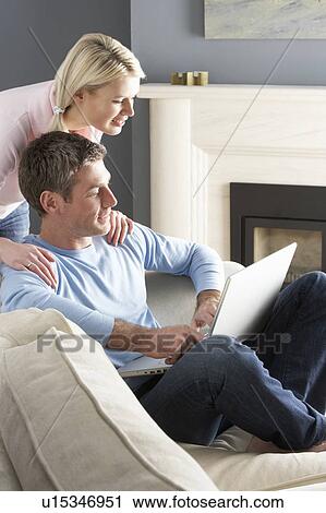 Stock Image - Couple Using Laptop Relaxing Sitting On Sofa At Home. Fotosearch