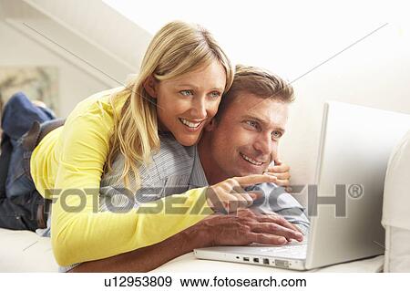Stock Photo - Couple Using Laptop Relaxing Sitting On Sofa At Home. Fotosearch