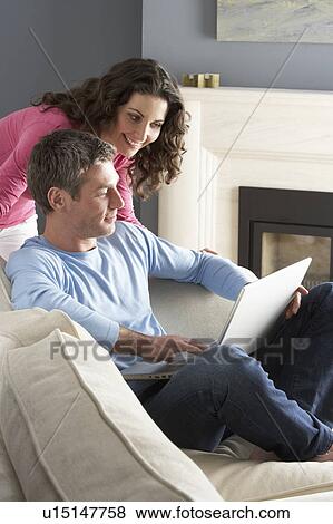 Couple Using Laptop Relaxing Sitting On Sofa At Home View Large Photo Image Stock Photo - Couple Using Laptop Relaxing Sitting On Sofa At Home. Fotosearch
