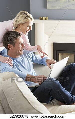Stock Photo - Couple Using Laptop Relaxing Sitting On Sofa At Home. Fotosearch