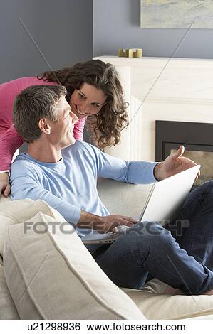 Couple Using Laptop Relaxing Sitting On Sofa At Home View Large Photo Image Stock Photograph - Couple Using Laptop Relaxing Sitting On Sofa At Home. Fotosearch