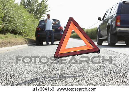 Stock Image - Driver Broken Down On Country Road With Hazard Warning Sign In Foreground. Fotosearch