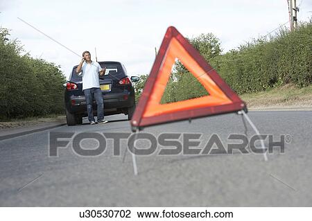 Stock Image - Driver Broken Down On Country Road With Hazard Warning Sign In Foreground. Fotosearch