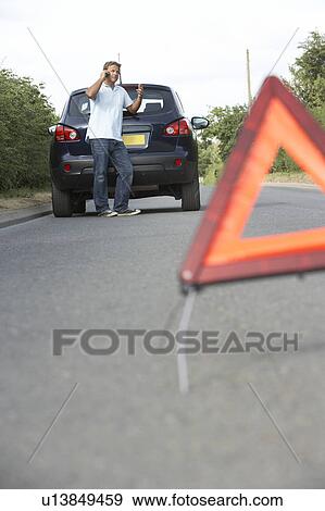 Stock Photo - Driver Broken Down On Country Road With Hazard Warning Sign In Foreground. Fotosearch