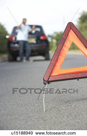 Stock Photo - Driver Broken Down On Country Road With Hazard Warning Sign In Foreground. Fotosearch