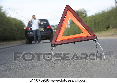 Stock Photograph - Driver Broken Down On Country Road With Hazard Warning Sign In Foreground. Fotosearch