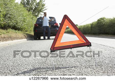 Stock Photograph - Driver Broken Down On Country Road With Hazard Warning Sign In Foreground. Fotosearch