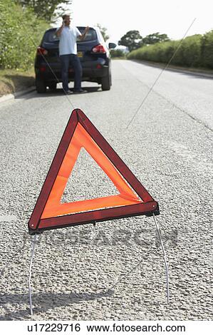 Stock Photograph - Driver Broken Down On Country Road With Hazard Warning Sign In Foreground. Fotosearch