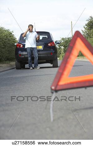 Stock Photograph - Driver Broken Down On Country Road With Hazard Warning Sign In Foreground. Fotosearch