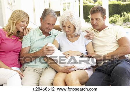 Stock Image - Extended Family Relaxing Together On Sofa With Newborn Baby. Fotosearch