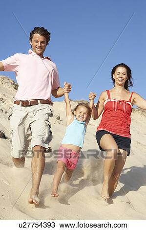 Stock Image - Family Enjoying Beach Holiday Running Down Dune. Fotosearch