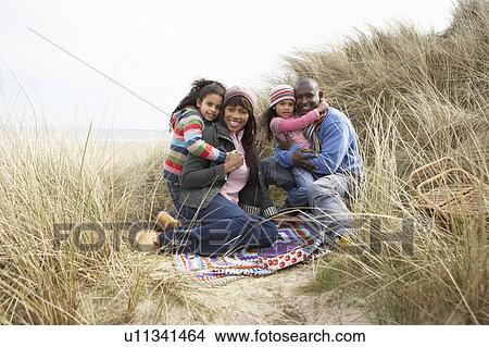 Picture - Family Sitting In Dunes Enjoying Picnic On Winter Beach. Fotosearch