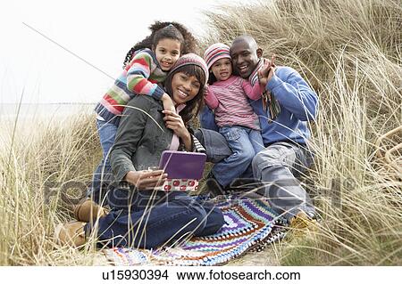 Picture - Family Sitting In Dunes Enjoying Picnic On Winter Beach. Fotosearch