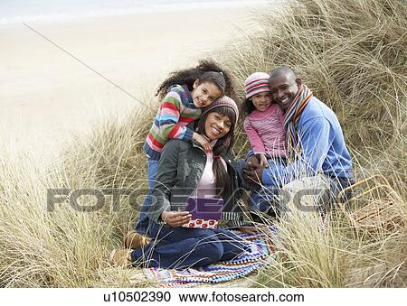 Stock Image - Family Sitting In Dunes Enjoying Picnic On Winter Beach. Fotosearch