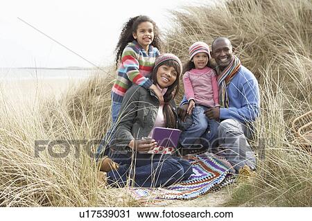Stock Image - Family Sitting In Dunes Enjoying Picnic On Winter Beach. Fotosearch