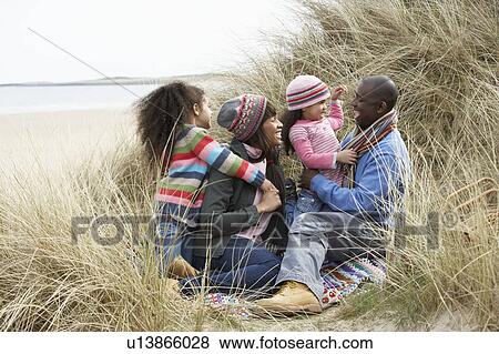 Stock Photo - Family Sitting In Dunes Enjoying Picnic On Winter Beach. Fotosearch