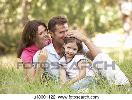 Stock Image - Family Sitting In Long Grass In Park. Fotosearch