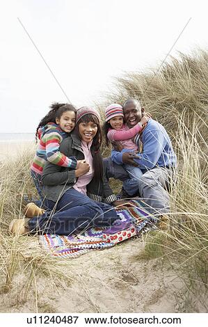 Stock Photo - Family Sitting On Blanket In Dunes On Winter Beach. Fotosearch
