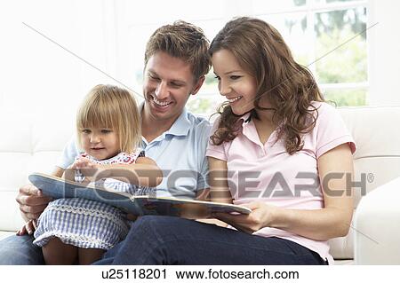 Stock Image - Family Sitting On Sofa Reading Book At Home. Fotosearch