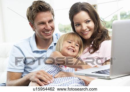 Stock Image - Family Sitting On Sofa Using Laptop At Home. Fotosearch