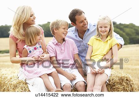 Stock Image - Family Sitting On Straw Bales In Harvested Field. Fotosearch