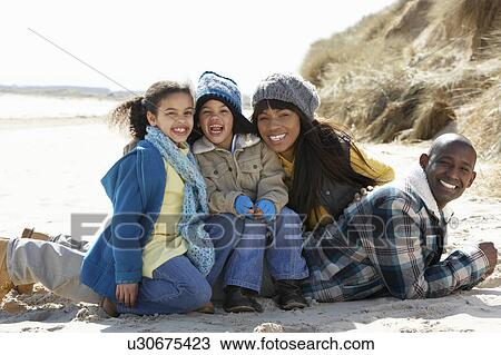 Stock Image - Family Sitting On Winter Beach. Fotosearch