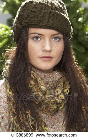 Stock Photo - Fashionable Teenage Girl Wearing Cap And Knitwear In Studio In Front Of Christmas Tree. Fotosearch