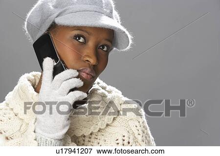 Stock Photo - Fashionable Woman Wearing Knitwear And Cap In Studio Using Mobile Phone. Fotosearch