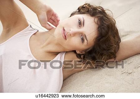 Stock Image - Fashionably Dressed Attractive Young Woman Laying Amongst Sand Dunes. Fotosearch